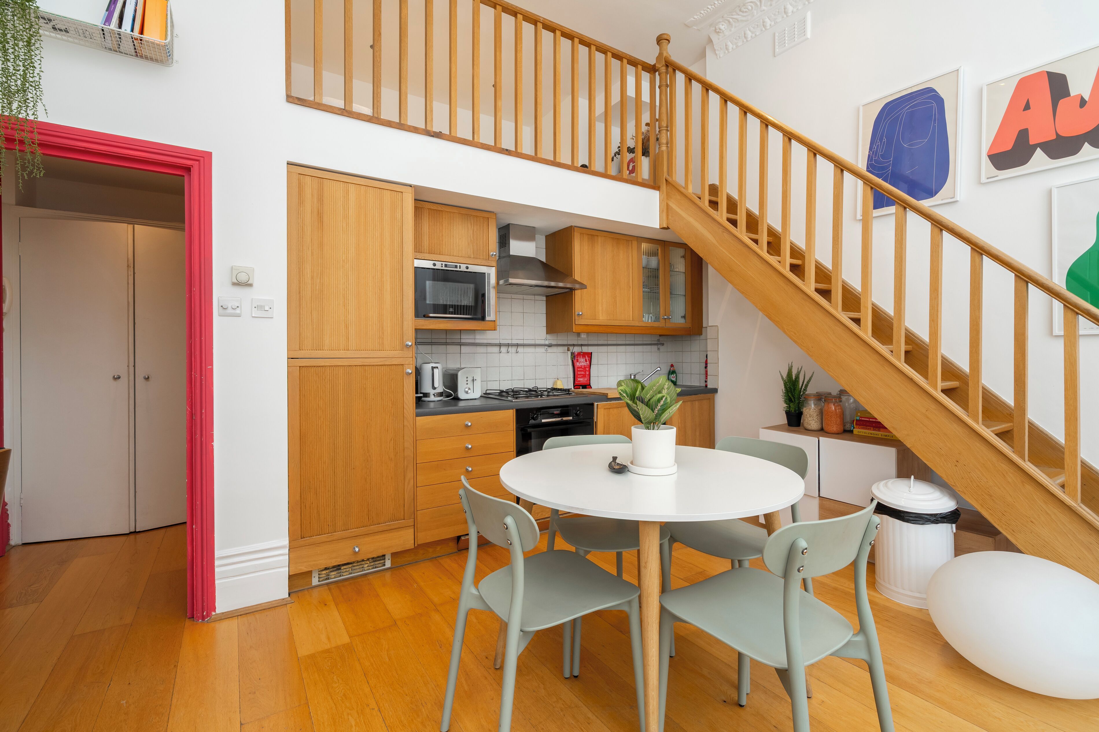 A modern kitchen with wooden cabinets, a round dining table, and a staircase.