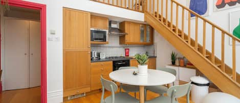 A modern kitchen with wooden cabinets, a round dining table, and a staircase.