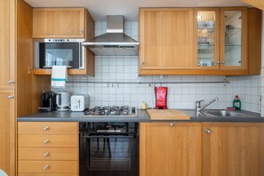 A kitchen with wooden cabinets, a stainless steel range hood, a built-in oven, a gas stove, a coffee maker, and a sink. - Perfect apartment in London close to top attractions and nightlife (London)