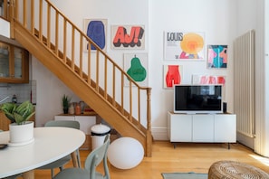 A modern living room with a wooden staircase, a dining area with a round table and chairs, and a TV on a white cabinet. - Perfect apartment in London close to top attractions and nightlife (London)