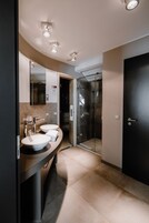 Un baño moderno con un tocador curvo, dos lavamanos, una cabina de ducha de vidrio y una puerta oscura.