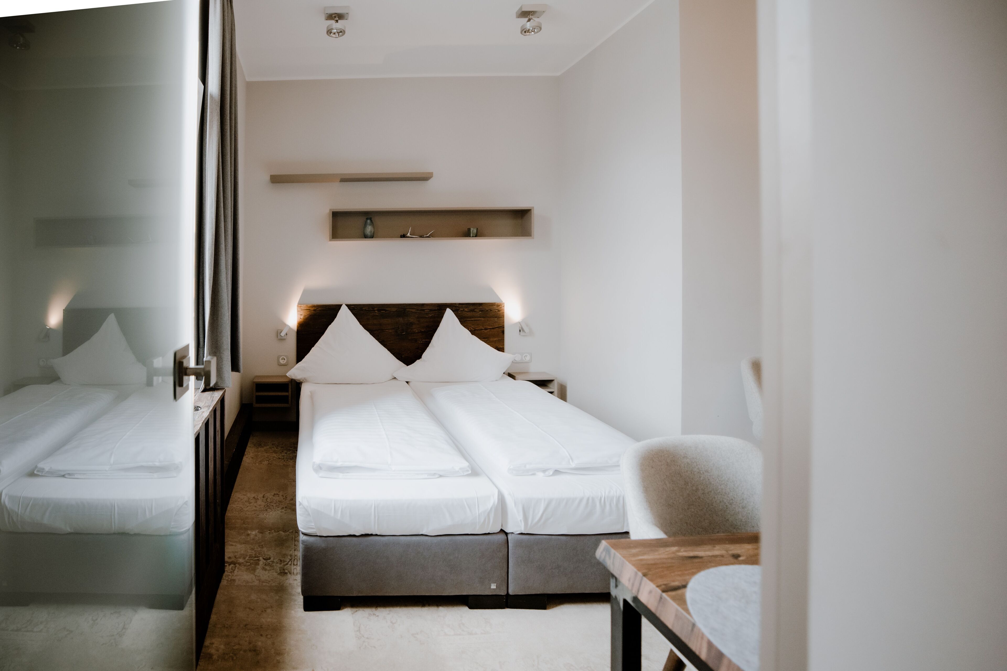 A modern hotel room with a large bed, bedside tables, a desk, and a mirror.