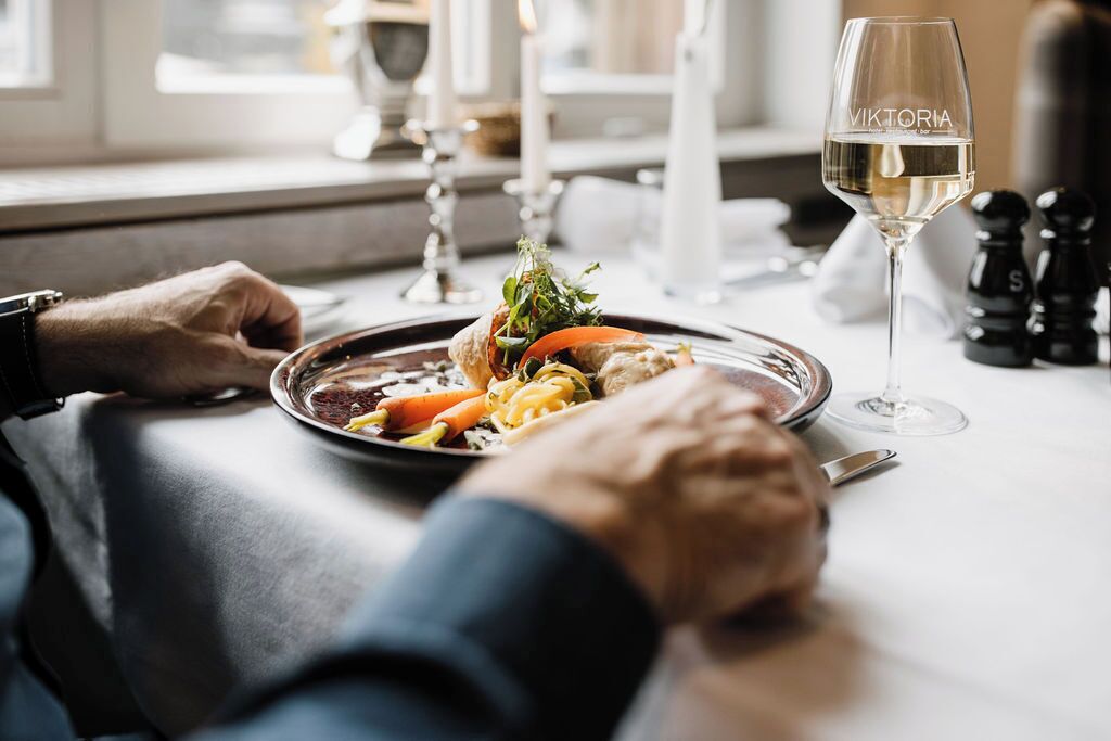 A dining table with a plate of food, a glass of white wine, and salt and pepper shakers.