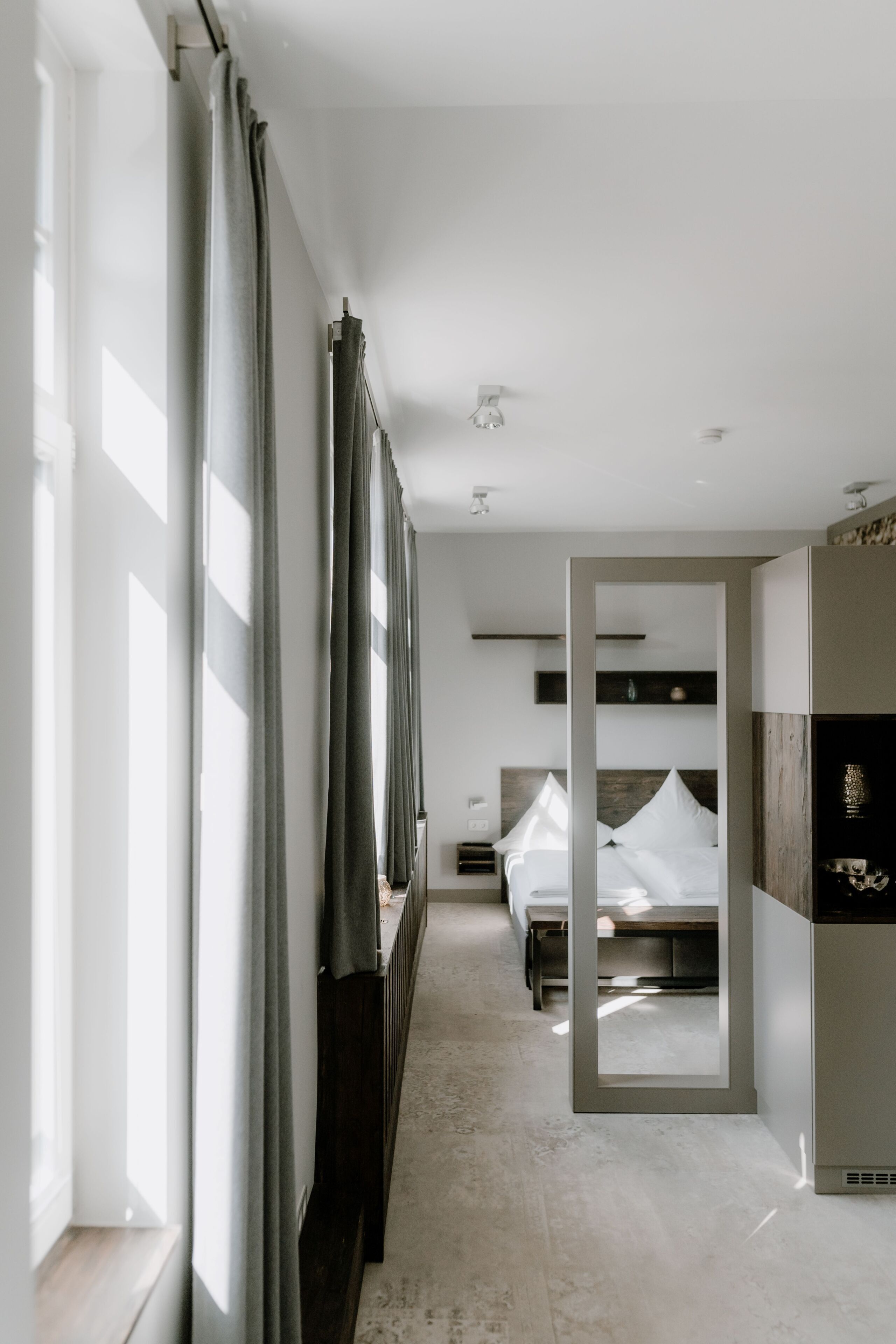 Ein modernes Hotelzimmer mit einem Bett, einem Nachttisch und einem großen Fenster mit Vorhängen.