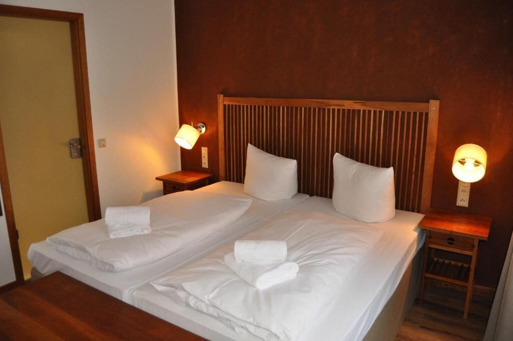 A double bed with white linens and two bedside lamps.