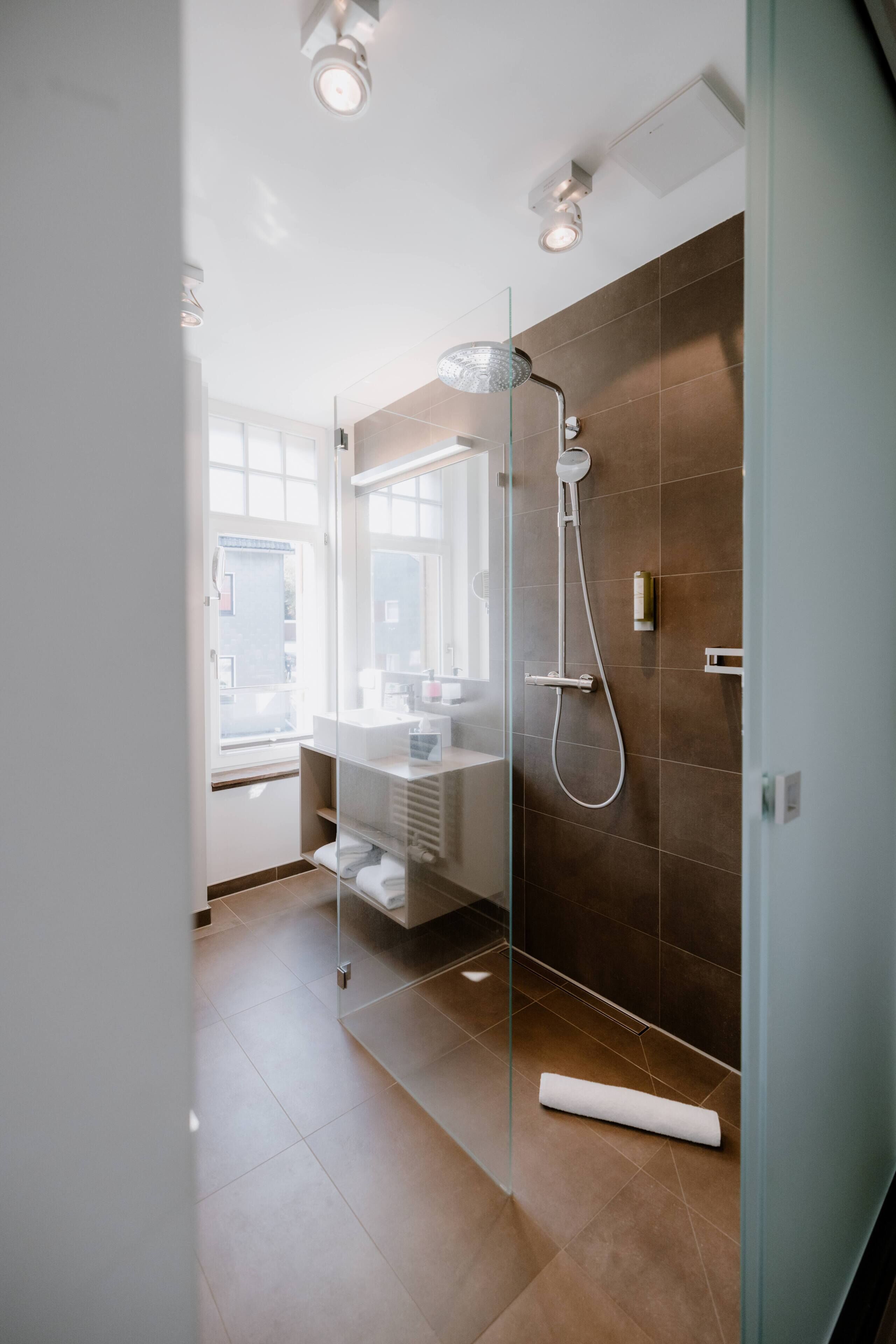 A modern bathroom with a glass shower enclosure, a vanity with a mirror, and a view of the outside.