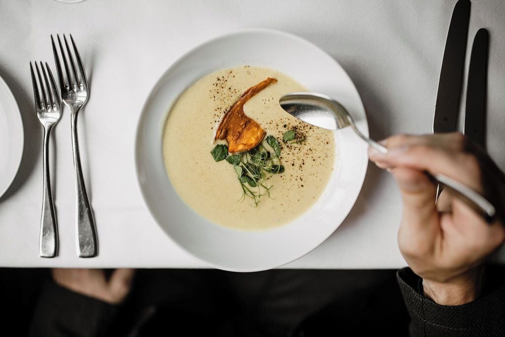 Una mesa de comedor con un plato de sopa, un tenedor, una cuchara y un cuchillo.