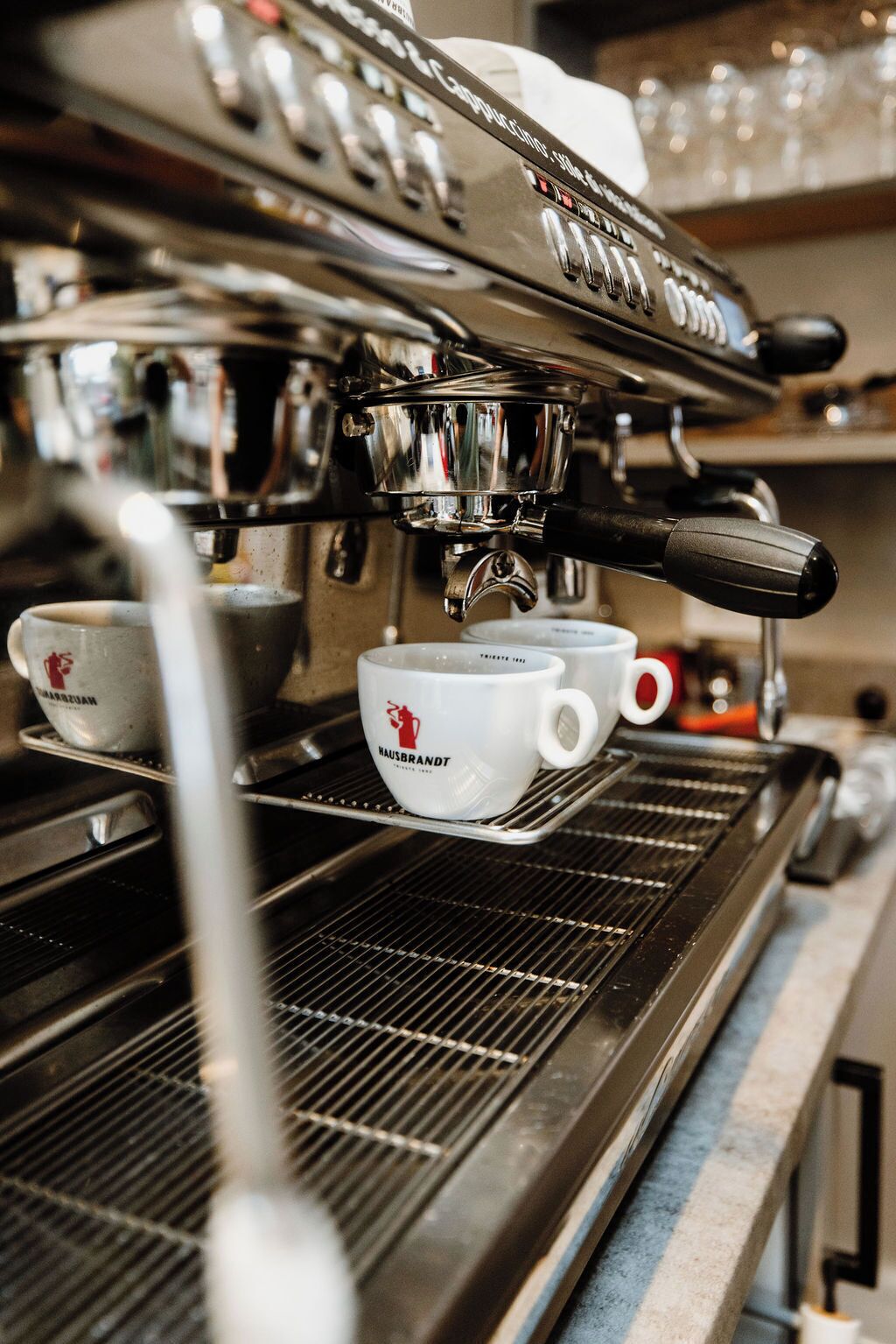 An espresso machine with a metal drip tray and two white cups with logos.