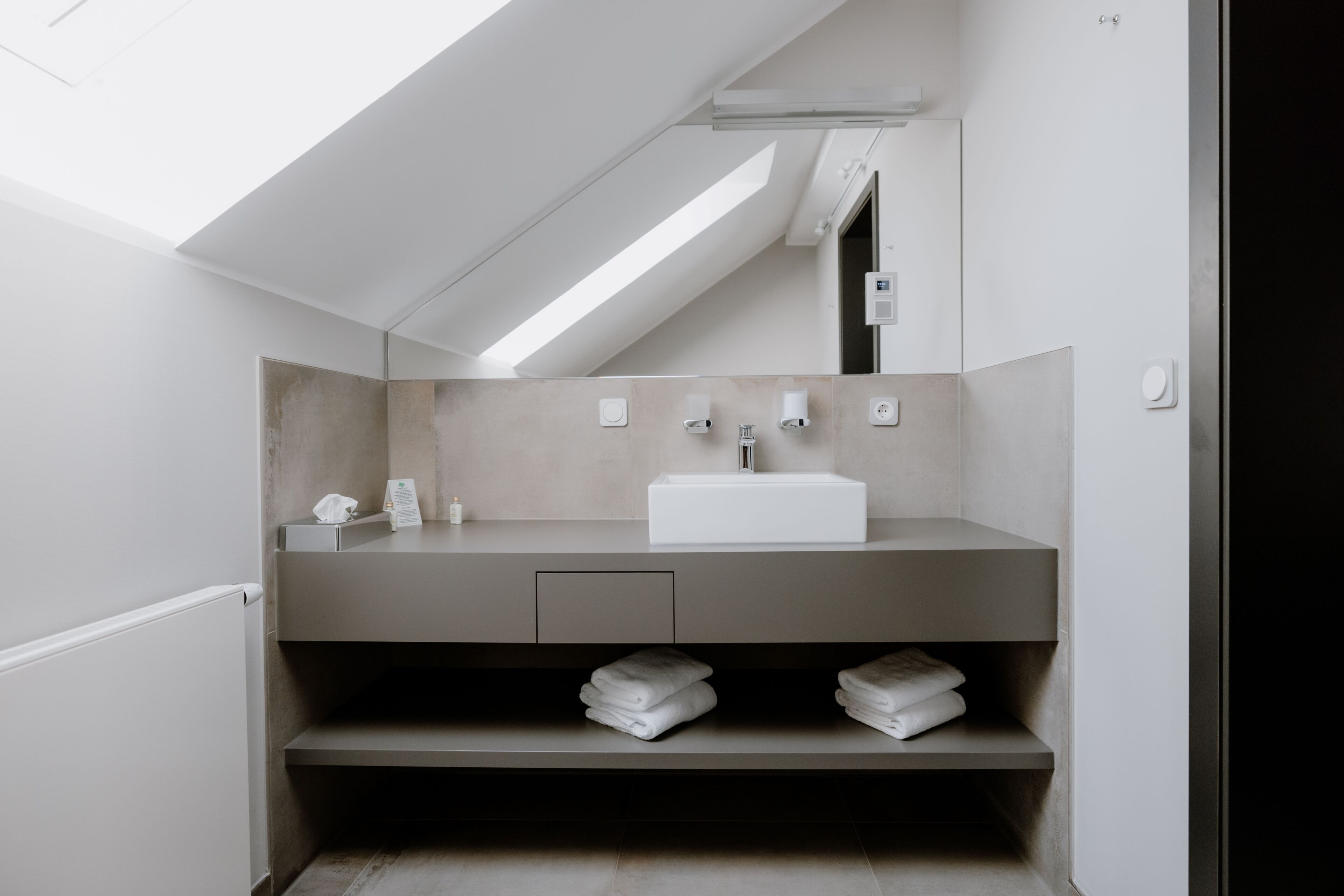 A modern bathroom with a skylight, a white sink, and a towel rack.