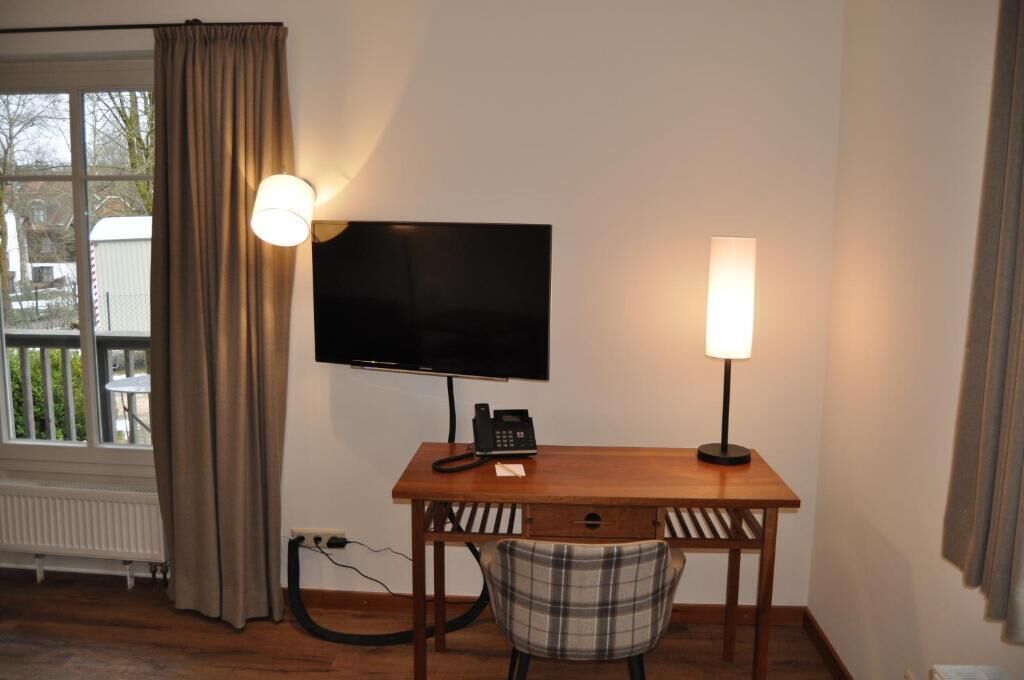 Ein Zimmer mit einem an der Wand befestigten Fernseher, einem Schreibtisch mit Telefon und einem Sessel.