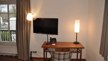 Ein Zimmer mit einem an der Wand befestigten Fernseher, einem Schreibtisch mit Telefon und einem Sessel.