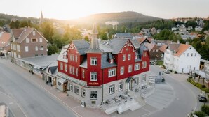 A red building with a sign 'VIKTORIA' at the entrance, located at a street corner with a view of a hill in the background. - StrandBerg's Designhotel Viktoria (Braunlage)