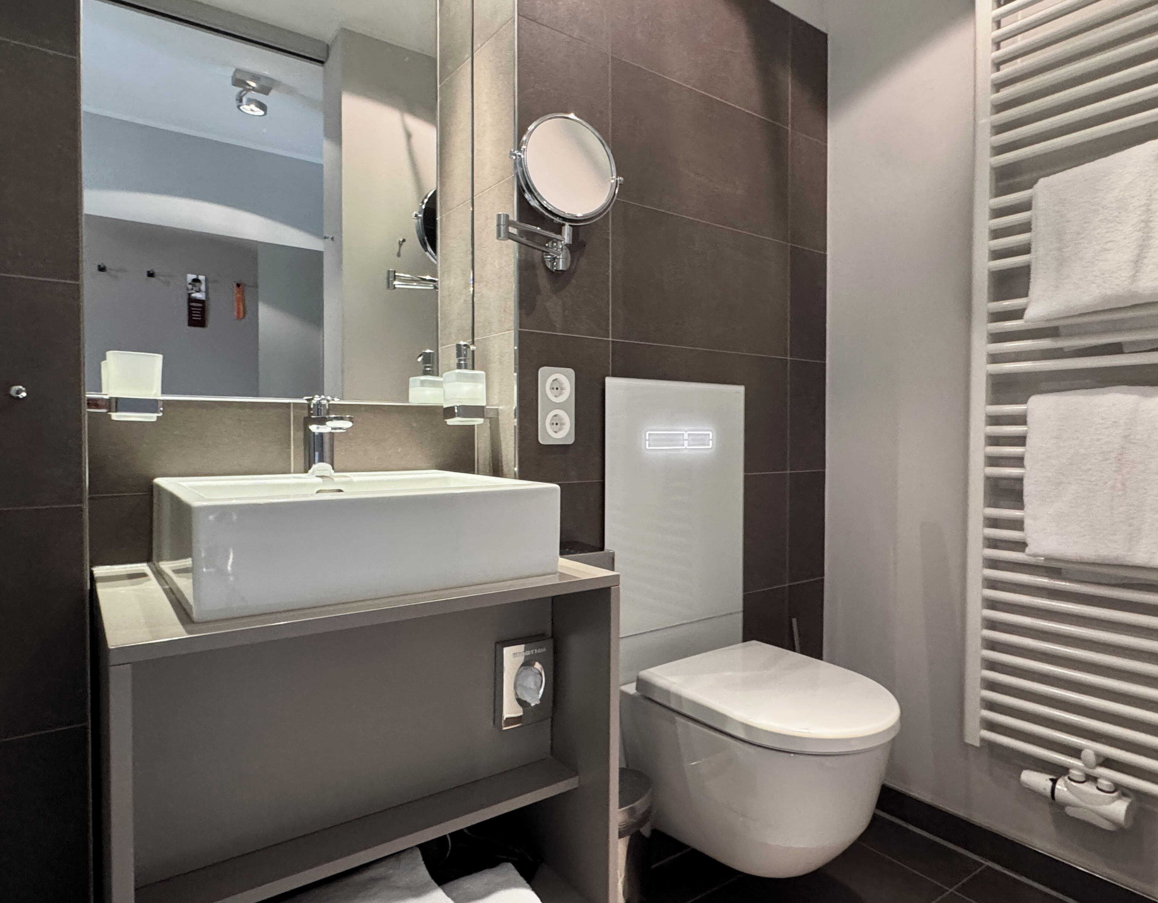A modern bathroom with a sink, mirror, toilet, and towel rack.