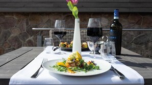 A table set with a plate of food, wine glasses, a bottle of wine, and a vase with a flower. - StrandBerg's Designhotel Viktoria (Braunlage)