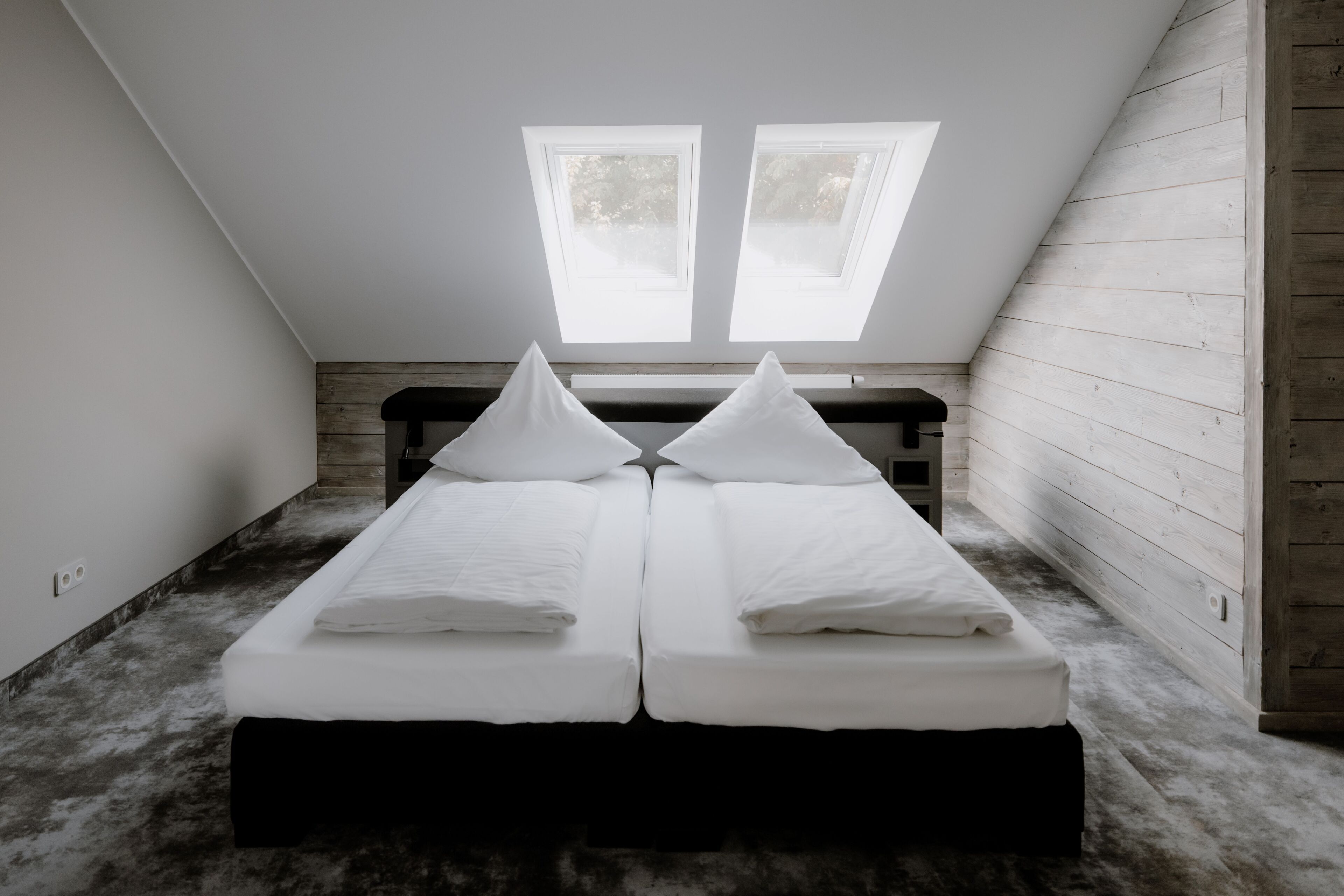 Ein Zimmer mit zwei Einzelbetten, einer Sitzbank und Dachfenstern.