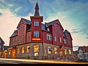 Un edificio grande de ladrillo rojo con numerosas ventanas y una torre destacada, señalado como hotel y restaurante.