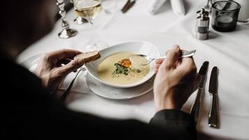 A person dining with a bowl of soup and bread, a glass of white wine, and cutlery on a table.