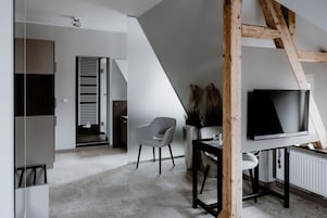 Un interior moderno con un televisor montado en la pared, una silla gris y una escalera que conduce a otra habitación.