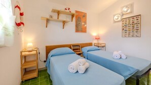 A hotel room with two beds, a wooden headboard, a shelf with decorative items, a wall art of a ghost, a fish-themed wall chart, and a green tiled floor. - Margherite Apartments by Wonderful Italy (Porto Ottiolu)