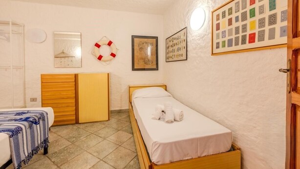 A small, clean room with a single bed, a wooden wardrobe, a small table, and a wall-mounted shelf. - Margherite Apartments by Wonderful Italy (Porto Ottiolu)