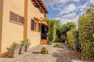 Un patio con un edificio, un sendero de piedra, plantas en macetas y una puerta de madera.