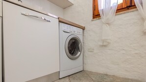 A compact laundry room with a front-loading washing machine and a cabinet. - Margherite Apartments by Wonderful Italy (Porto Ottiolu)