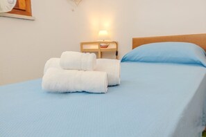 En seng med et blåt sengetæppe og to hvide, sammenrullet håndklæder på.