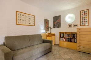 A living room with a sofa, a wooden desk, a bookshelf, and various framed pictures on the walls.