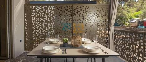 Un espace extérieur aménagé pour les repas, avec une table dressée pour quatre personnes, entourée de chaises en osier.