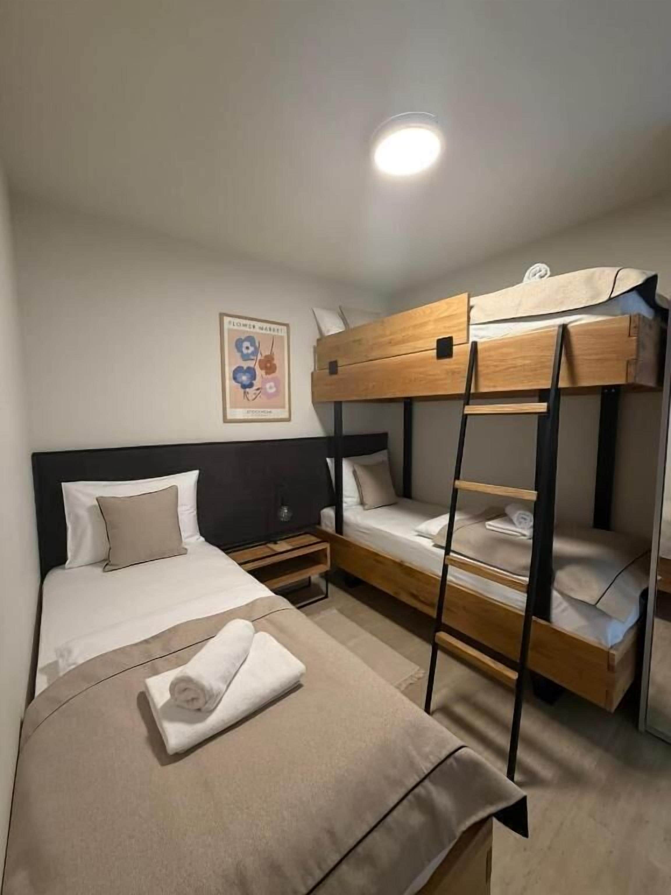 Quarto com beliche e uma cama de solteiro à esquerda, e o beliche à direita. Um criado-mudo com uma luminária fica entre as camas.