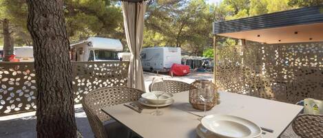 Un espace de restauration en plein air avec une table dressée pour deux personnes, entourée de chaises en osier et agrémentée d’un panier décoratif.