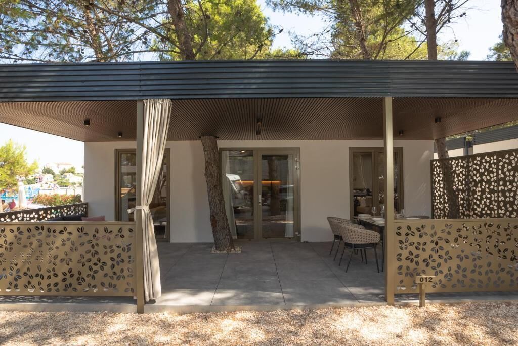 A covered outdoor seating area with a table and chairs, a glass door entrance, and a decorative fence.