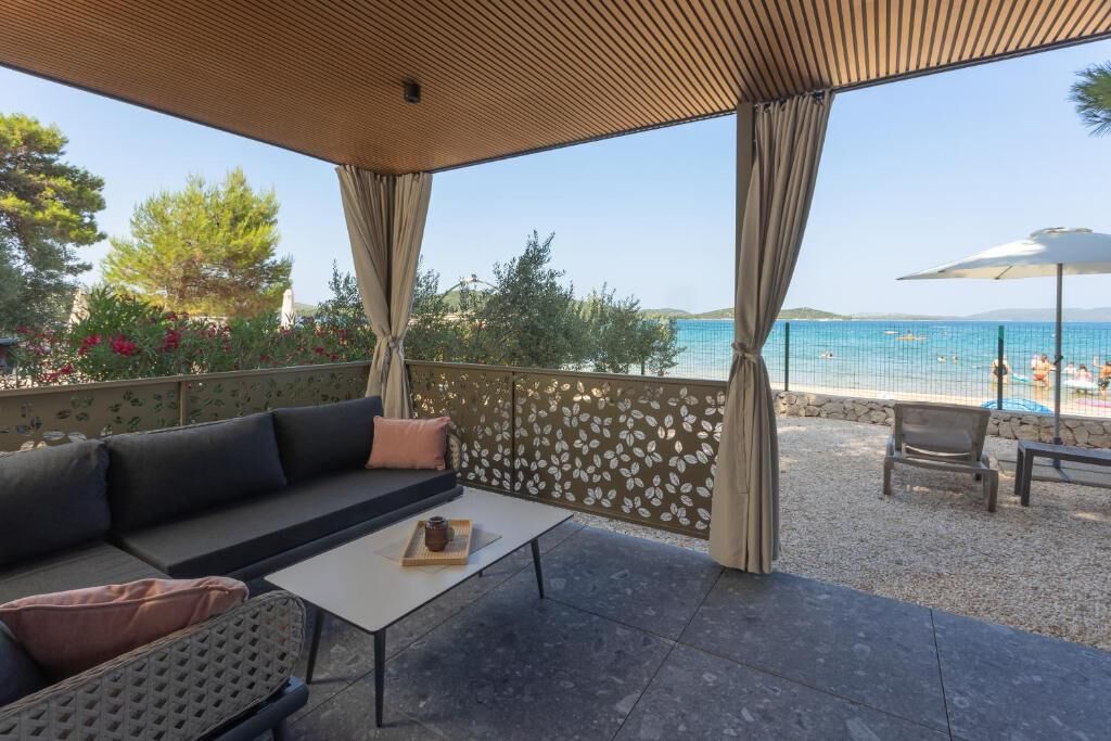 A covered outdoor seating area with a view of a beach and pool.