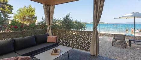 A covered outdoor seating area with a view of a beach and pool.