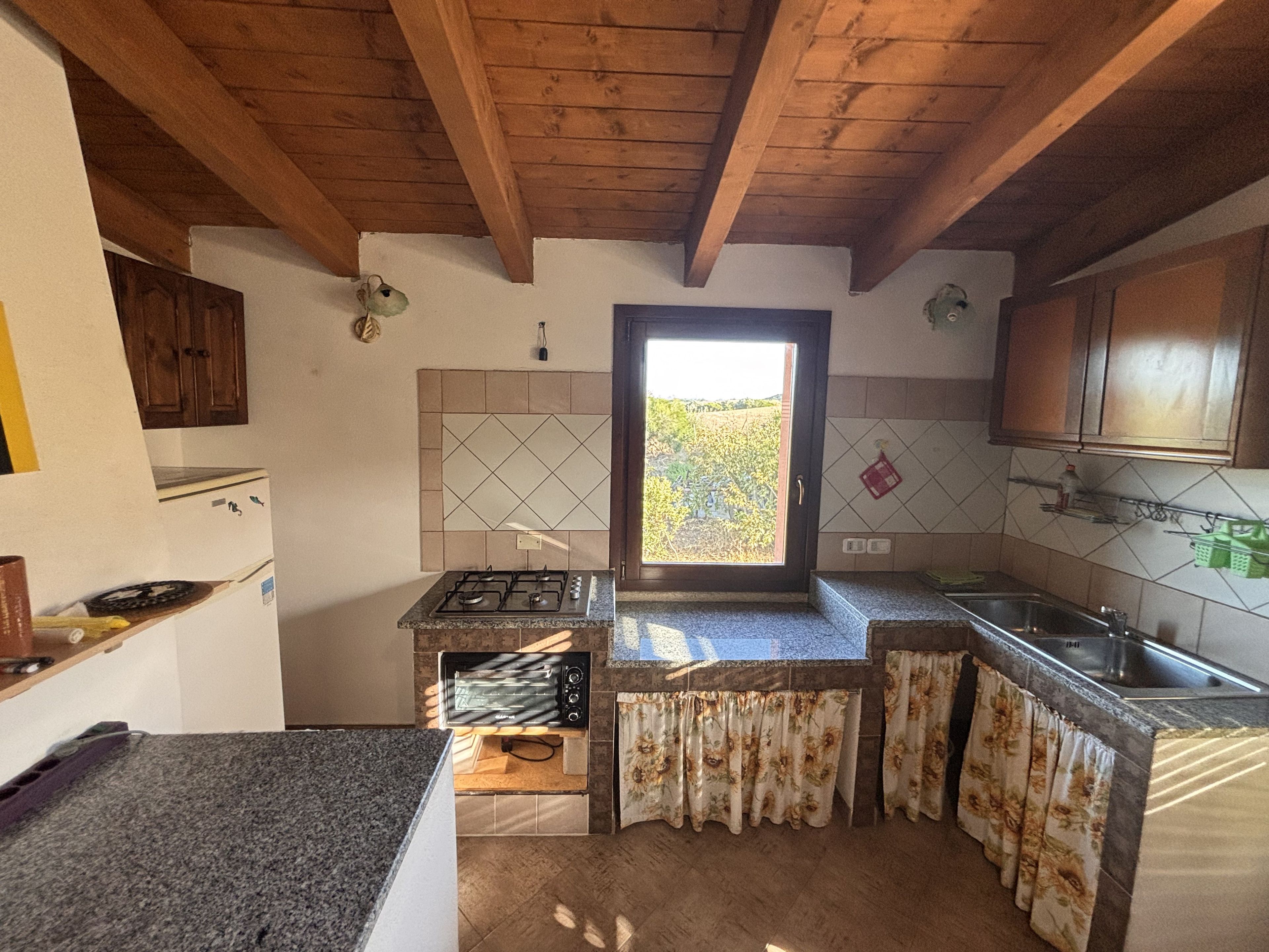 A kitchen with a gas stove, a built-in oven, a sink, and wooden ceiling beams.