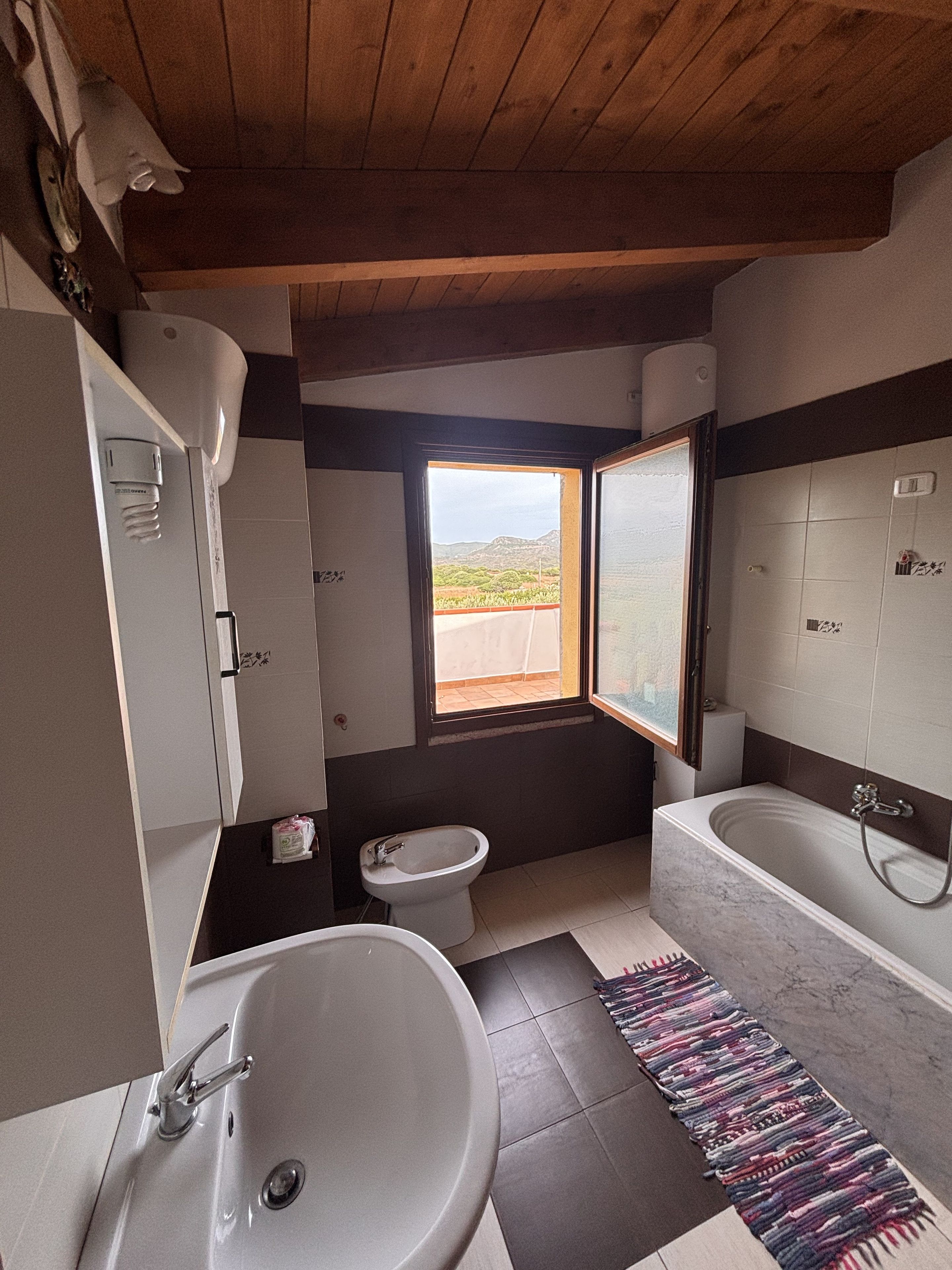Un bagno con un lavandino capiente, bidet e vasca da bagno. Una finestra offre vista sull'esterno.