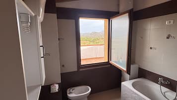 Un bagno con un lavandino capiente, bidet e vasca da bagno. Una finestra offre vista sull'esterno.