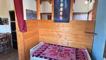 Ein Zimmer mit Holzboden, einem Bett mit gemustertem Überwurf, einem roten Vorhang und einer Wand mit einem Poster.