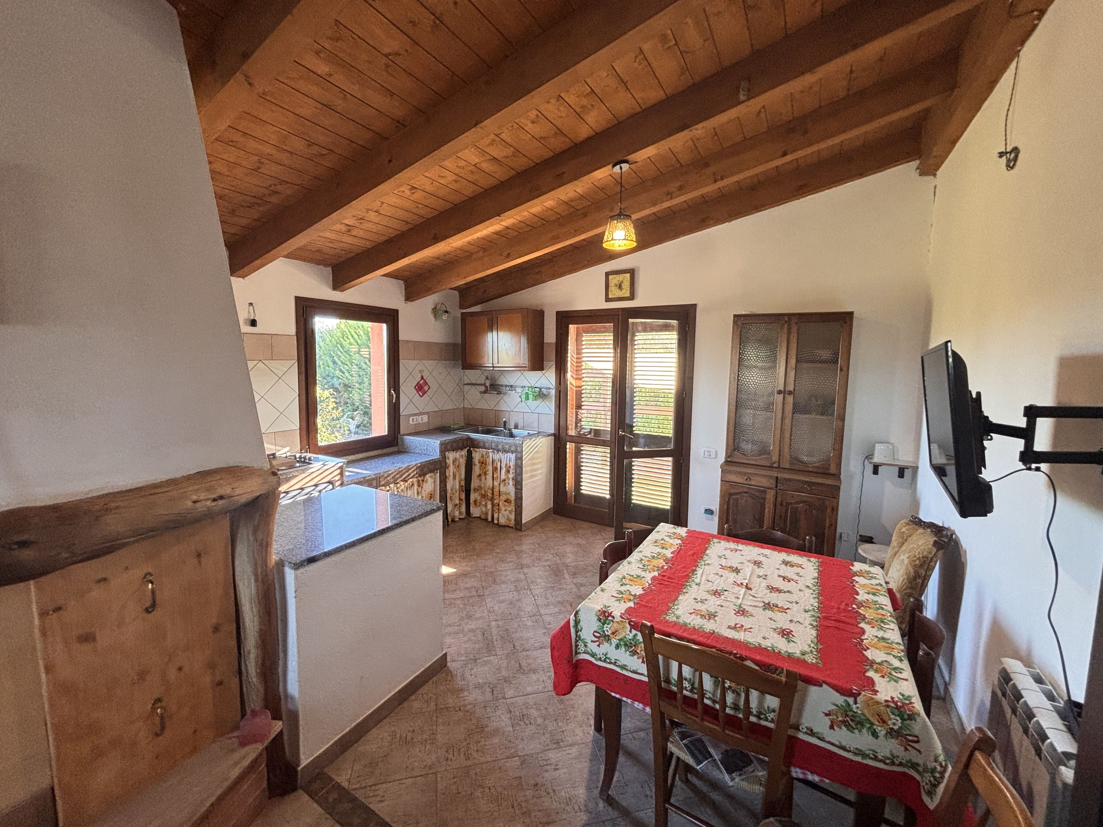 Una cucina compatta con soffitto in legno, un tavolo da pranzo con tovaglia e una televisione montata a parete.