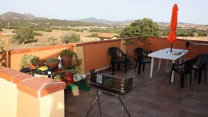Une terrasse avec une table et des chaises, entourée de plantes en pot et d’un barbecue.