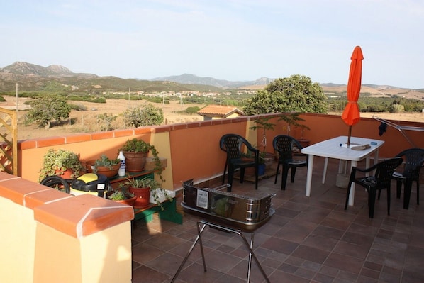 Un patio con mesa y sillas, rodeado de plantas en macetas y una parrilla.