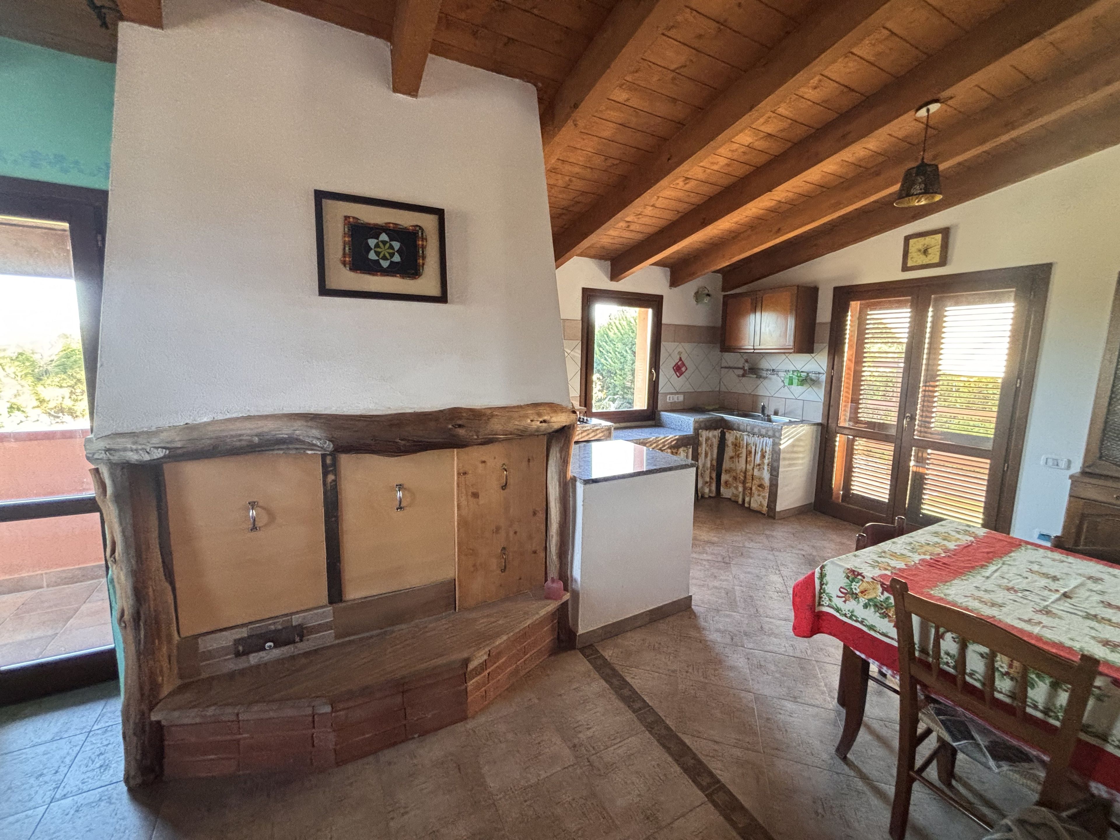 A kitchen with wooden cabinets, a built-in bench, a dining table with a tablecloth, and a view through the window.
