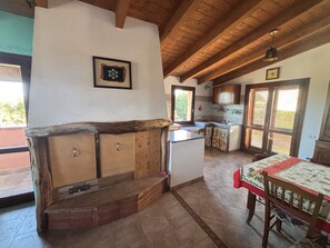 A kitchen with wooden cabinets, a built-in bench, a dining table with a tablecloth, and a view through the window.