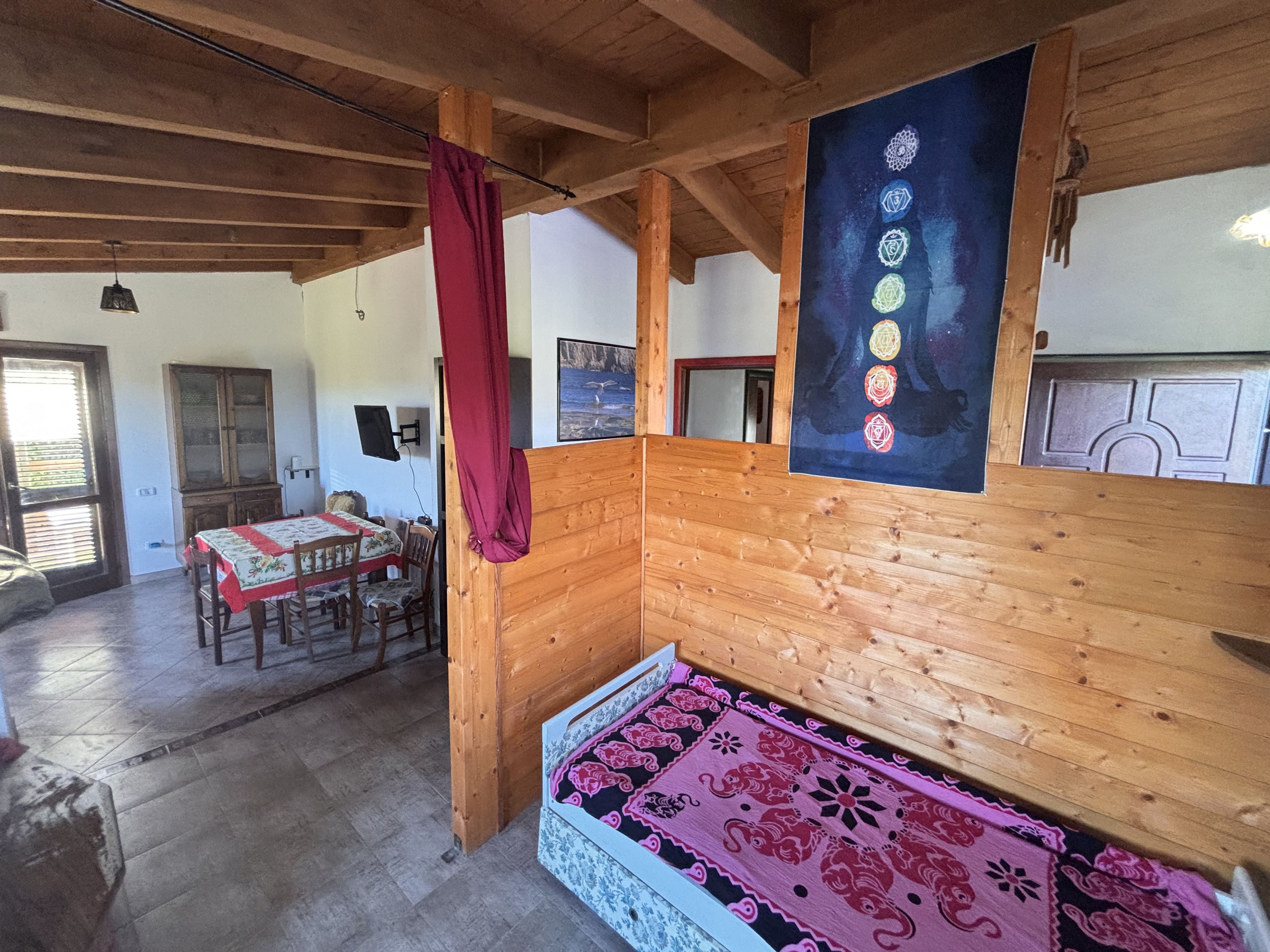 Une pièce avec un plafond en bois, un lit recouvert d’une couvre-lit à motifs, une table à manger avec des chaises et un buffet.