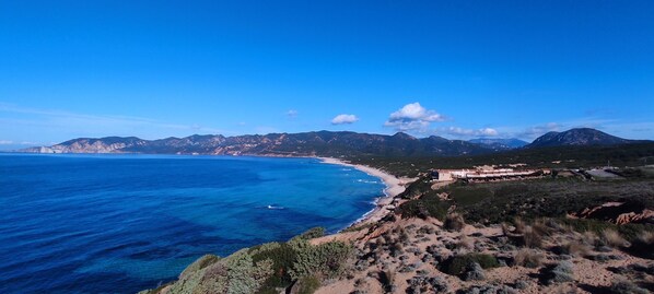 A coastal landscape with a clear view of the sea, a beach, and a mountainous backdrop.