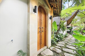 A wooden door with intricate carvings, a stone pathway, and lush greenery. - Sakara Bali Villa by Kozystay - Ubud (Kabupaten Gianyar)