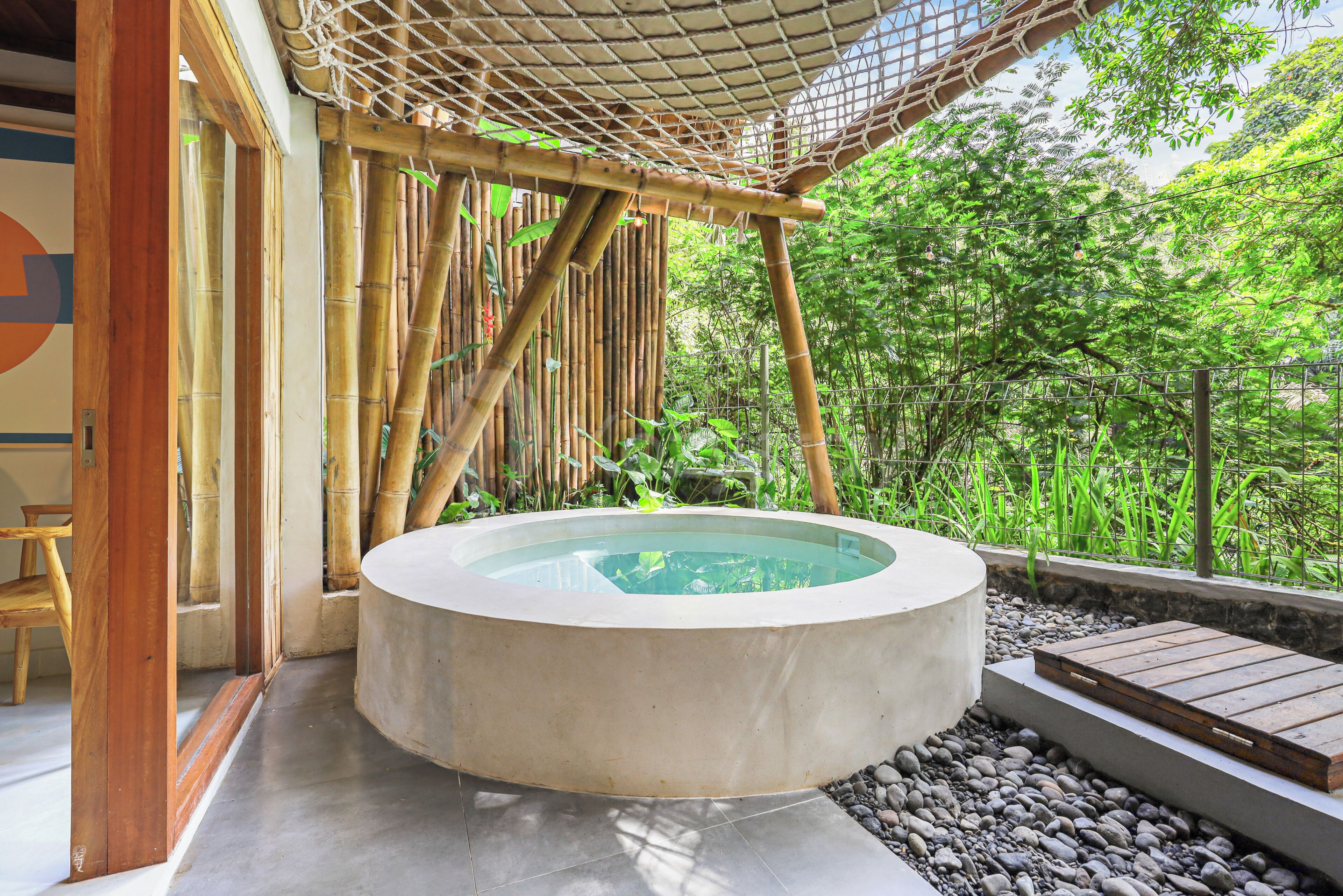 A hot tub in a covered outdoor area with bamboo structures and a view of lush greenery.