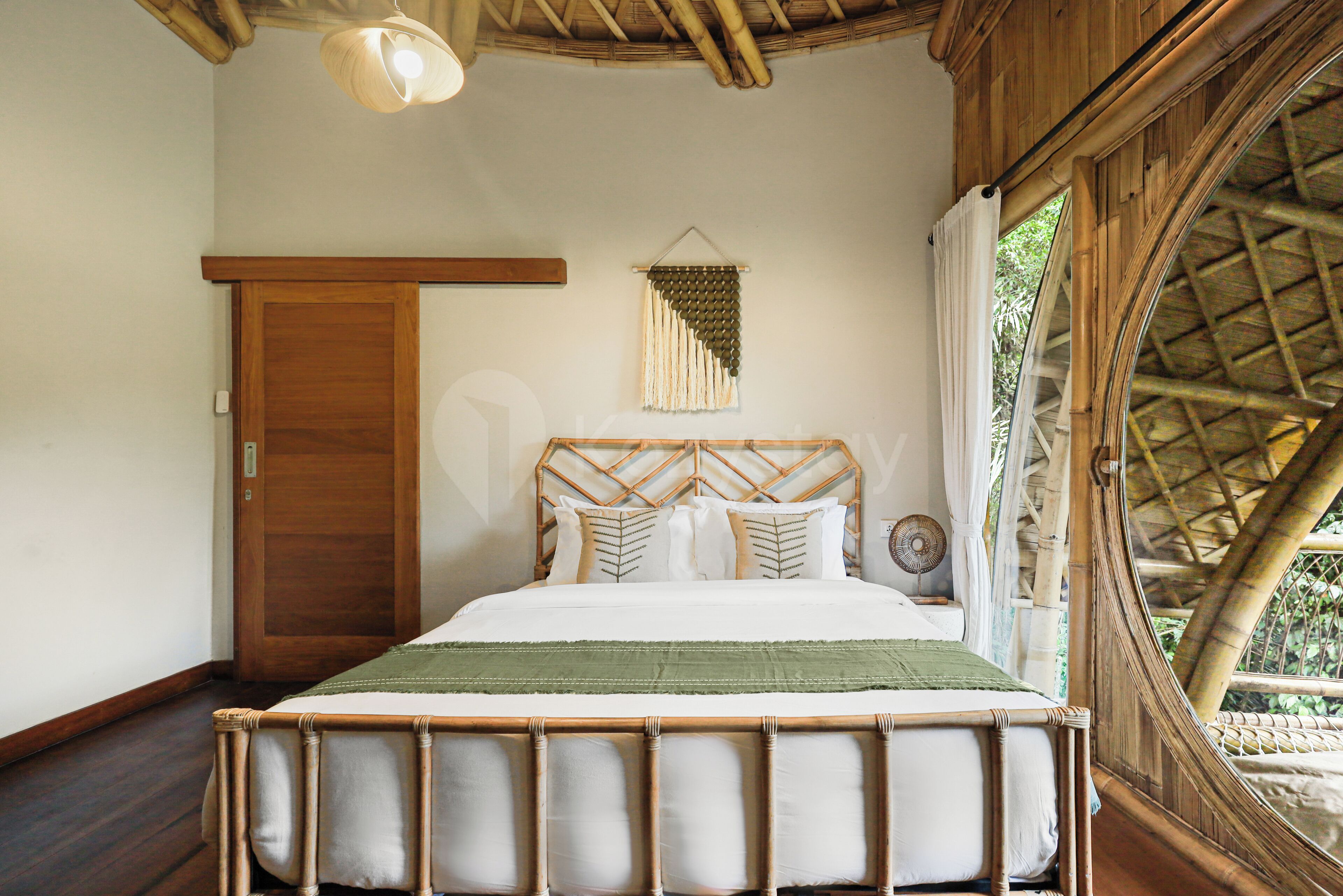 Een kamer met een bed, een houten deur, een wanddecoratie en een raam met uitzicht op groen.