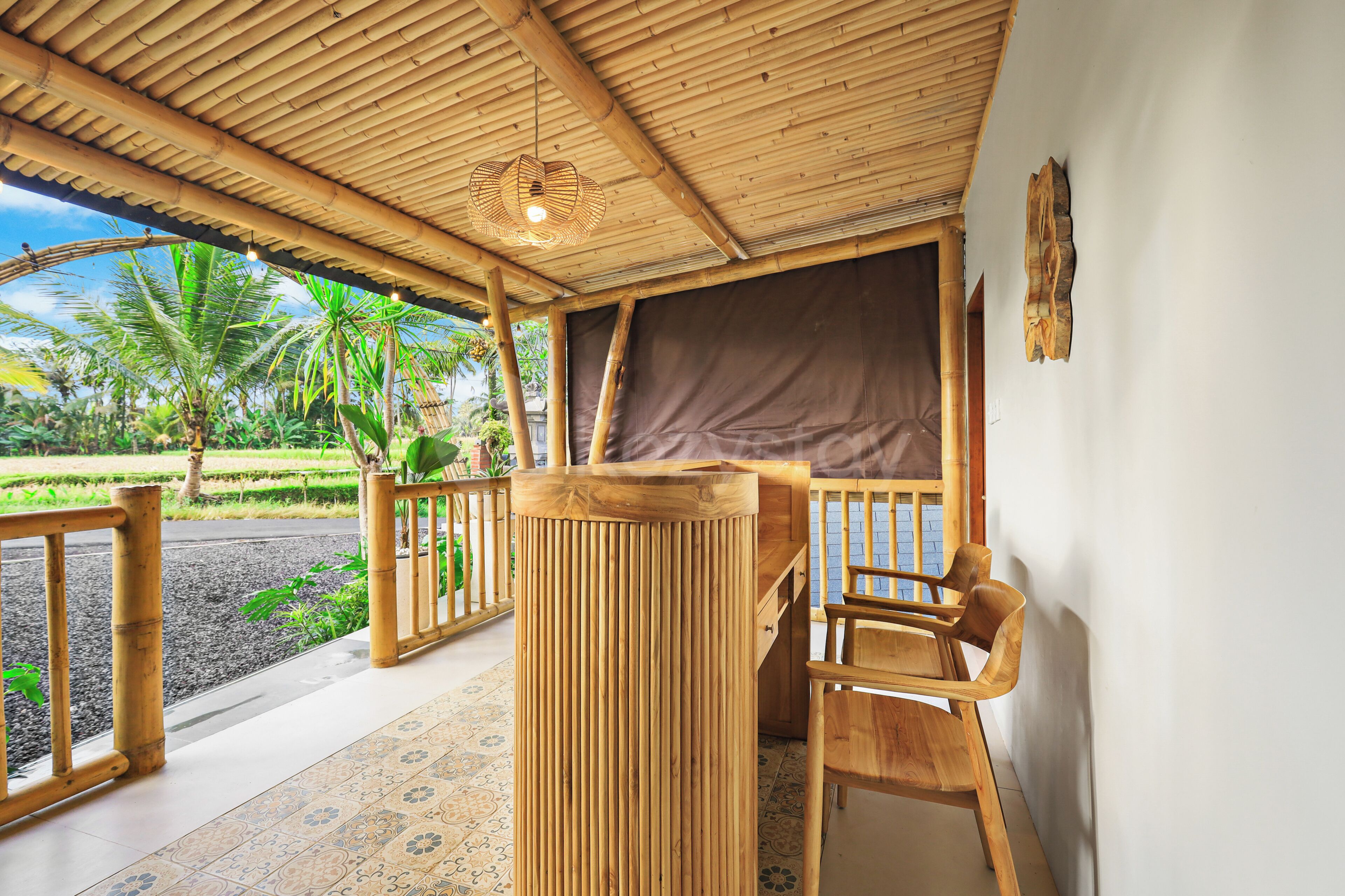 Un área de estar al aire libre con madera, que incluye una mesa y sillas, techo de bambú y vistas a un jardín con palmeras.