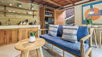 Una cocina moderna con armarios de madera, horno empotrado y comedor con sofá azul y mesa de madera.